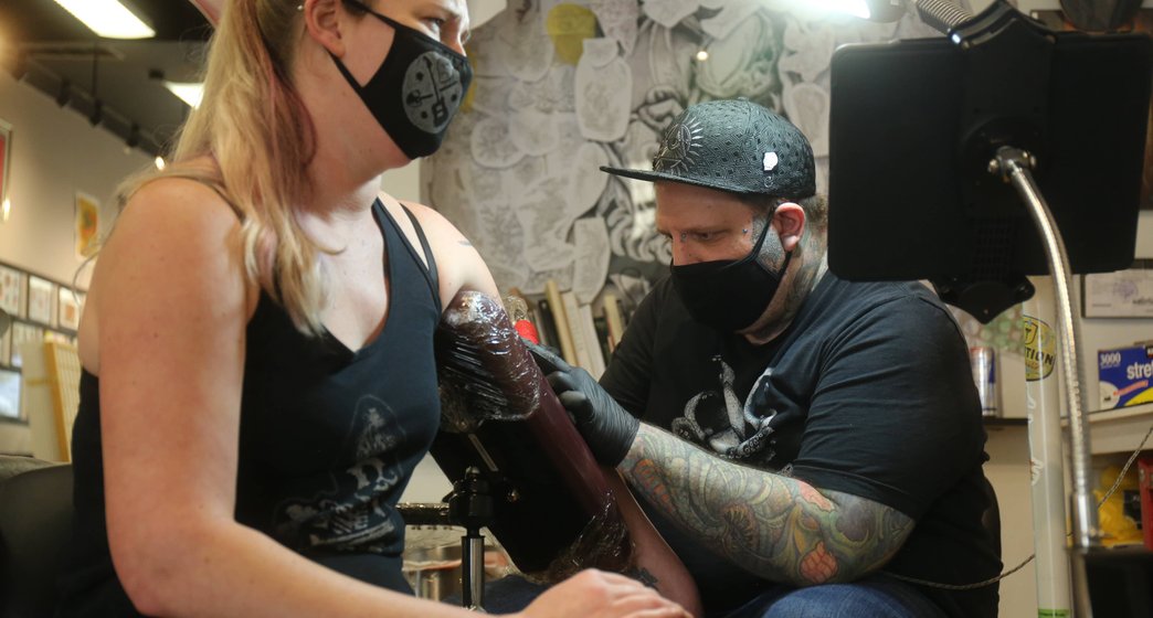 tattoo artist working on a womans arm in the studio